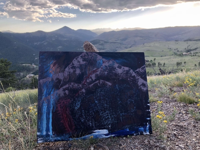 Blue and purple abstract mountain painting balanced on a rock at sunset